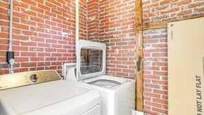 A laundry room with a white washer and dryer, a brick wall, and a 'DO NOT LAY FLAT' sign. - Conveniently Located North Charleston Home! (North Charleston)