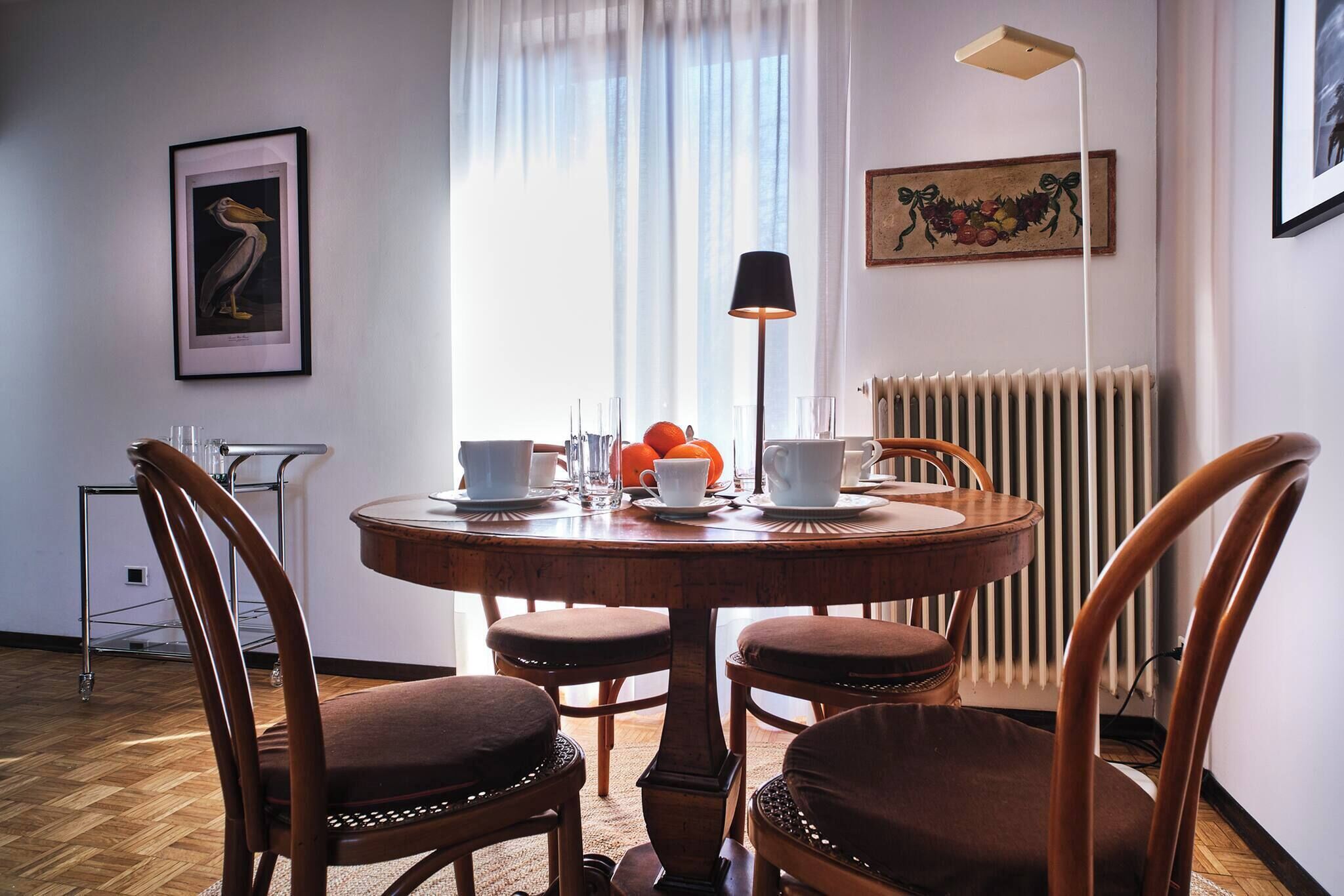 A dining area with a round table, four chairs, a lamp, and a radiator.