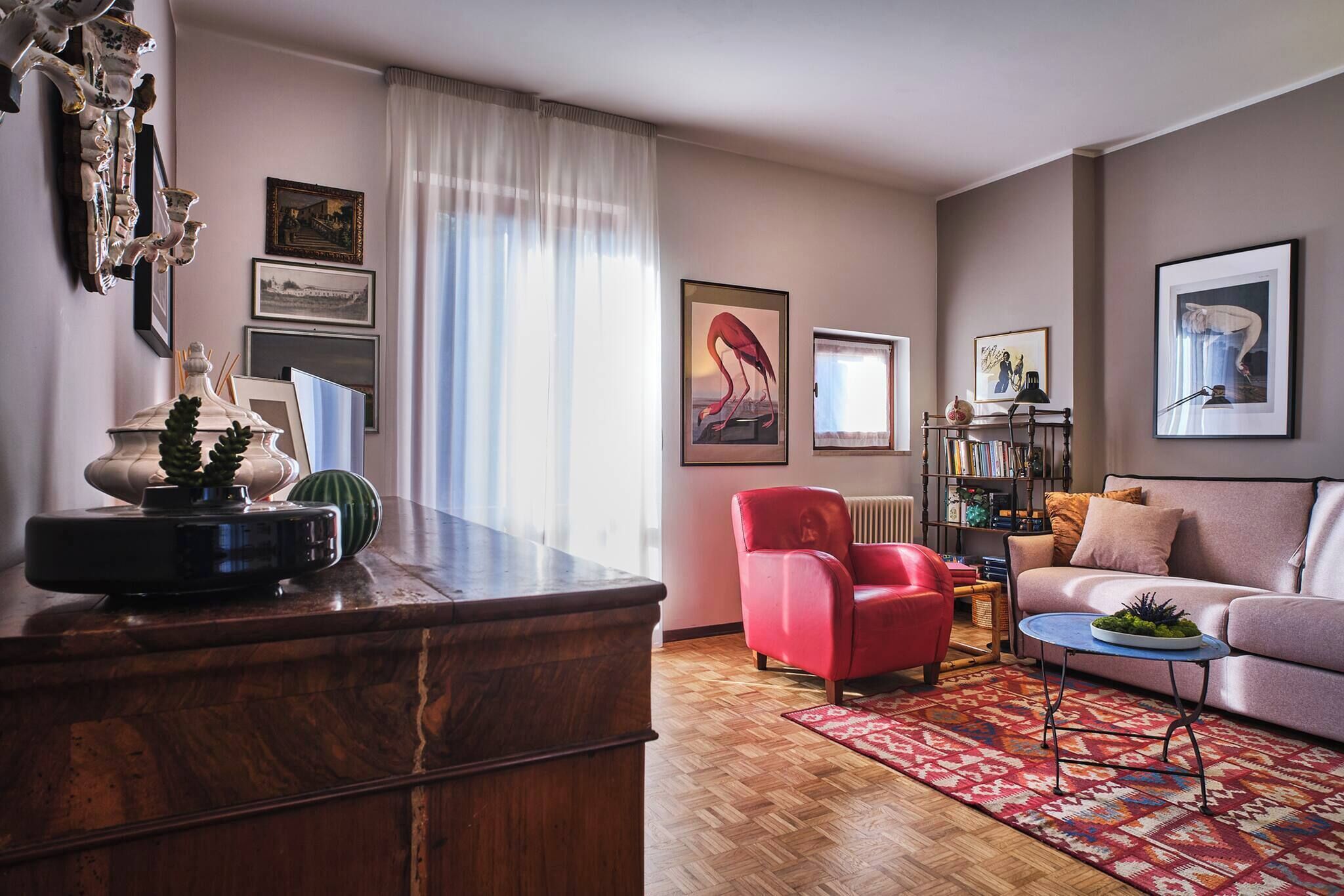 Een woonkamer met een houten salontafel, een rode fauteuil, een bank en een kamerkleed met een patroon.