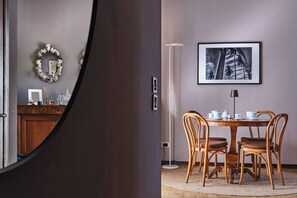 A dining area with a round table, four chairs, a floor lamp, and a framed picture on the wall.