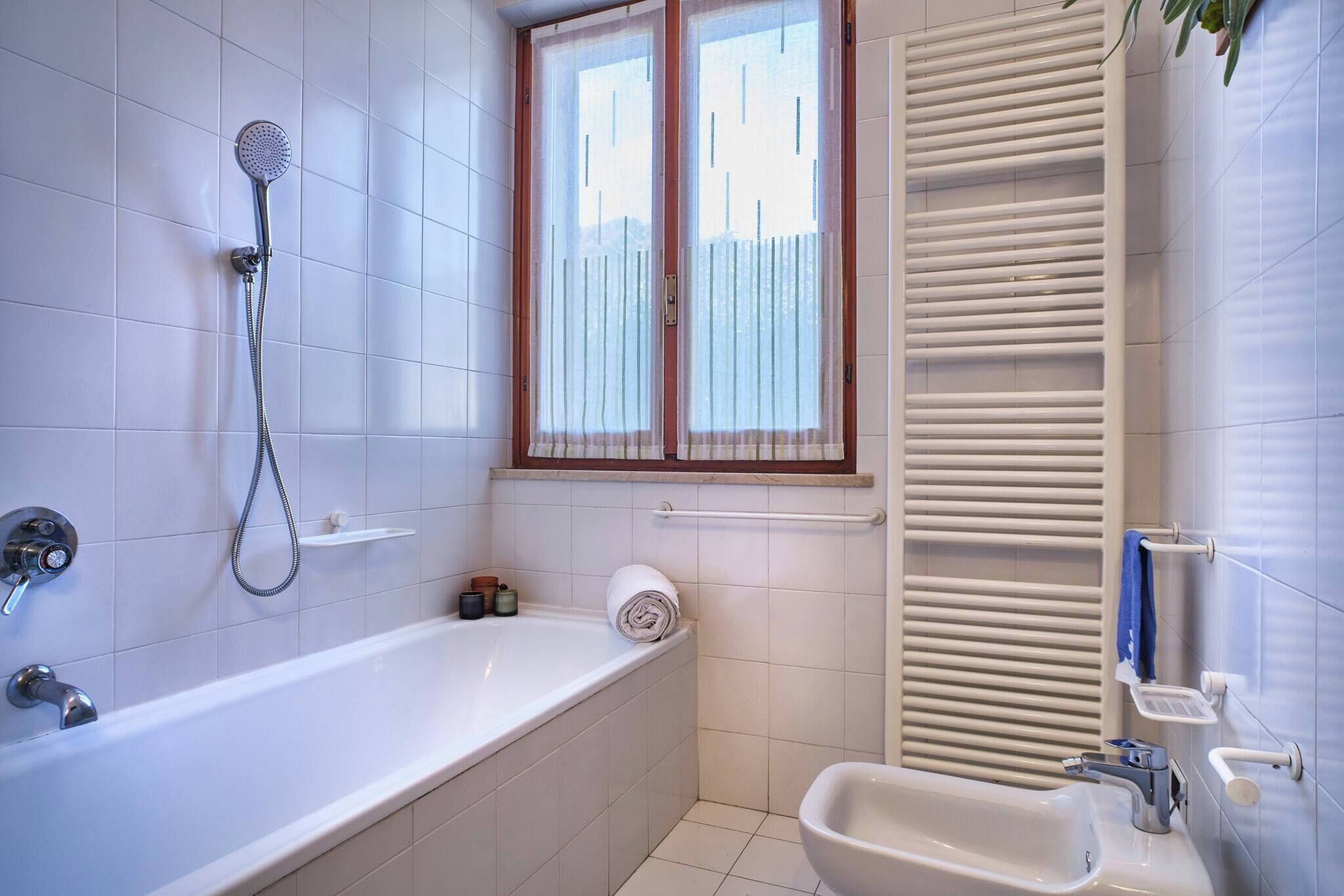 A modern bathroom with a bathtub, a shower, a toilet, and a window with curtains.