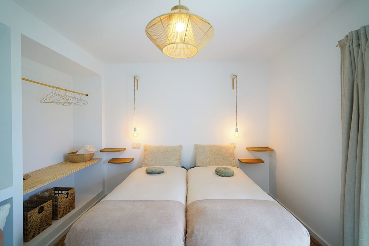 Un lit double avec deux tables de chevet, un luminaire suspendu et une étagère avec des paniers.