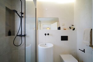 Un baño moderno con ducha de vidrio, lavamanos pedestal blanco y espejo sobre el lavamanos.