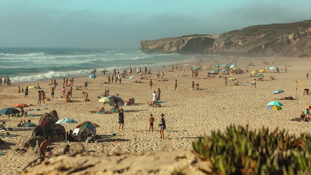 A crowded beach with people, umbrellas, and beach chairs.