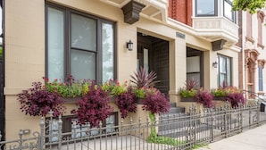 A row of townhouses with decorative planters on the exterior wall, a metal fence, and a sidewalk. - Urban Luxury on Washington Park | Rooftop & Parkin (Cincinnati)