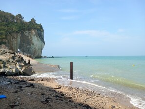 Una playa con costa rocosa, un muelle de madera y un acantilado cubierto de vegetación.