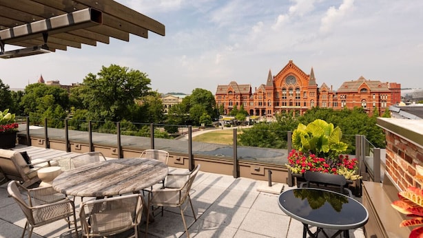 A terrace with a table and chairs, overlooking a large red building with a clock tower.