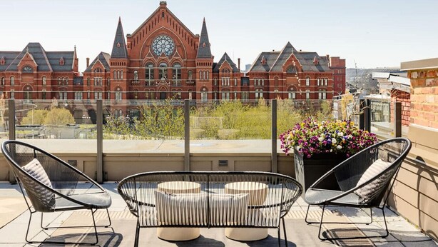 Een terras op het dak, met twee zwarte stoelen en een ronde tafel, met uitzicht op een historisch gebouw met een klokkentoren.