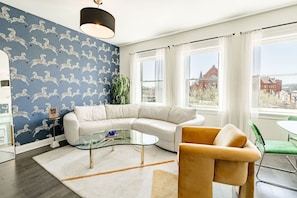 A modern living room with a white sectional sofa, a glass coffee table, and a green chair. - Downtown Cincinnati Stay | Rooftop Patio + Parking (Cincinnati)