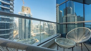 Un balcon avec vue sur le paysage urbain, comprenant des immeubles de grande hauteur et une rivière. On y trouve deux chaises en osier blanches.