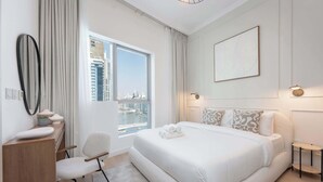 Une chambre d’hôtel moderne dotée d’un grand lit, offrant une vue sur le paysage urbain, d’un bureau avec une chaise et d’une petite table avec une lampe.
