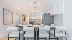 Une cuisine moderne avec des meubles blancs, un îlot central doté de tabourets de bar et un coin repas avec une table blanche dressée pour quatre personnes.