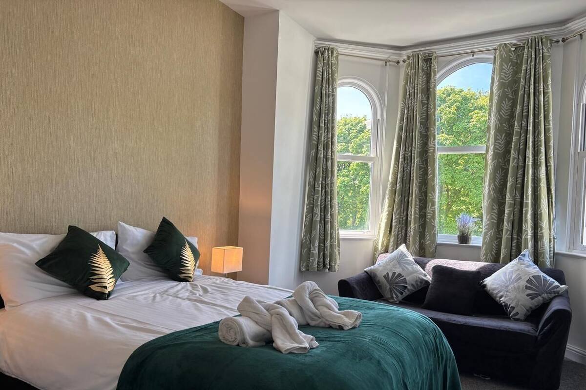A hotel room with a bed, a sofa, and a window with curtains.
