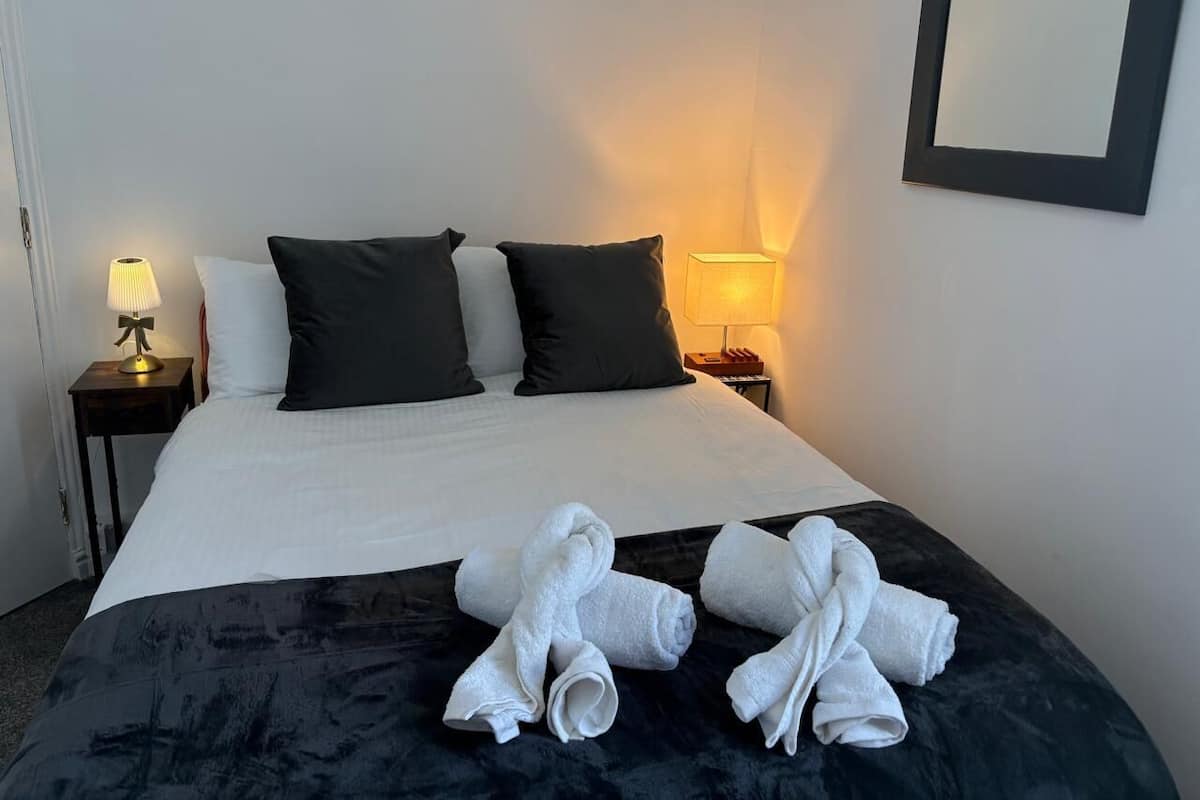A neatly made bed with white and black bedding, two bedside lamps, and a pair of towels on the bed.