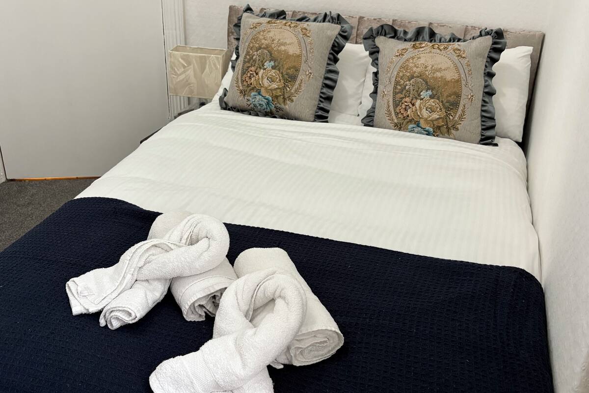 A neatly made bed with a white comforter, two decorative pillows, and a dark blue throw blanket.