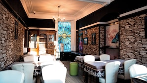 Un restaurant aux murs de pierre, aux chaises blanches et orné d’une fenêtre à vitraux.