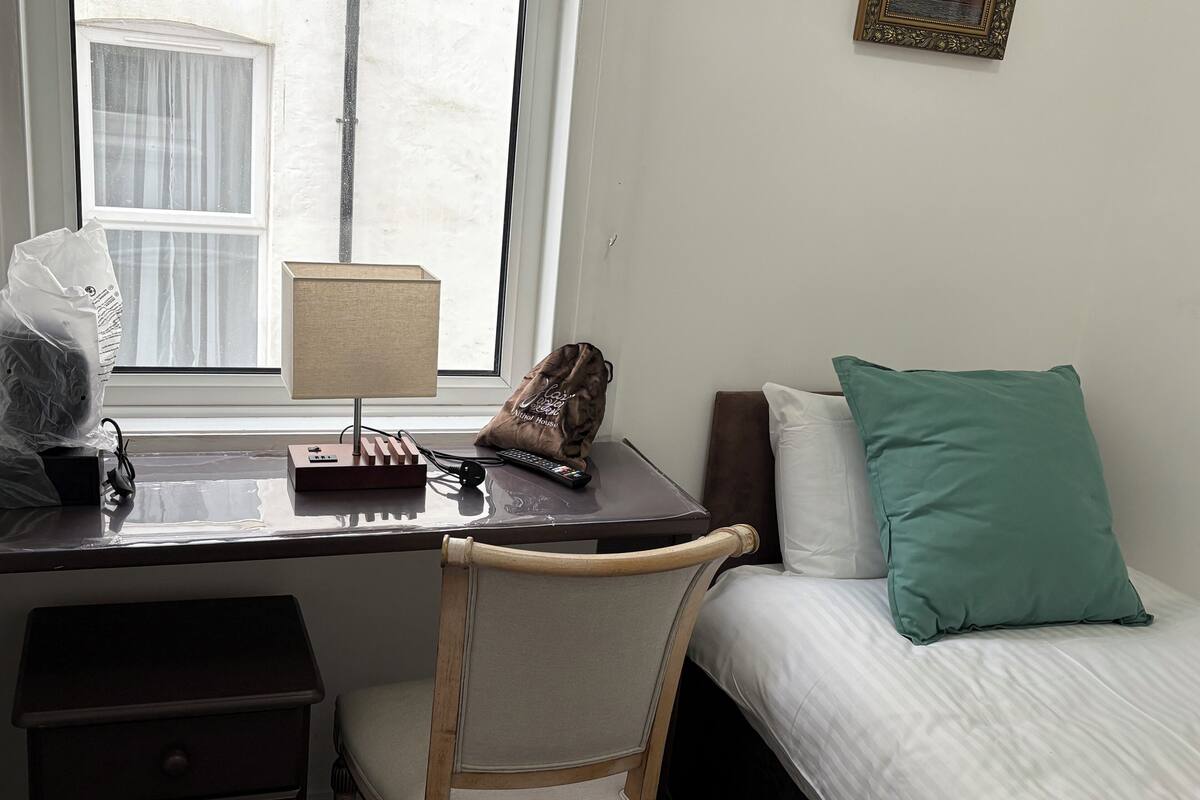 A hotel room with a desk, chair, bed, and a window.