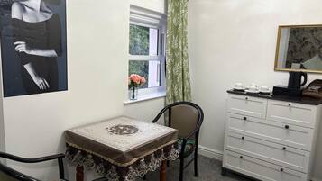 Una habitación pequeña con una mesa, una silla, un aparador, una ventana con cortina y un cuadro en la pared.