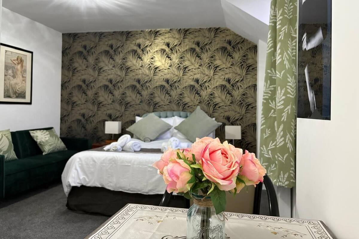 A bedroom with a bed, a green sofa, a vase with flowers, and a patterned wallpaper.