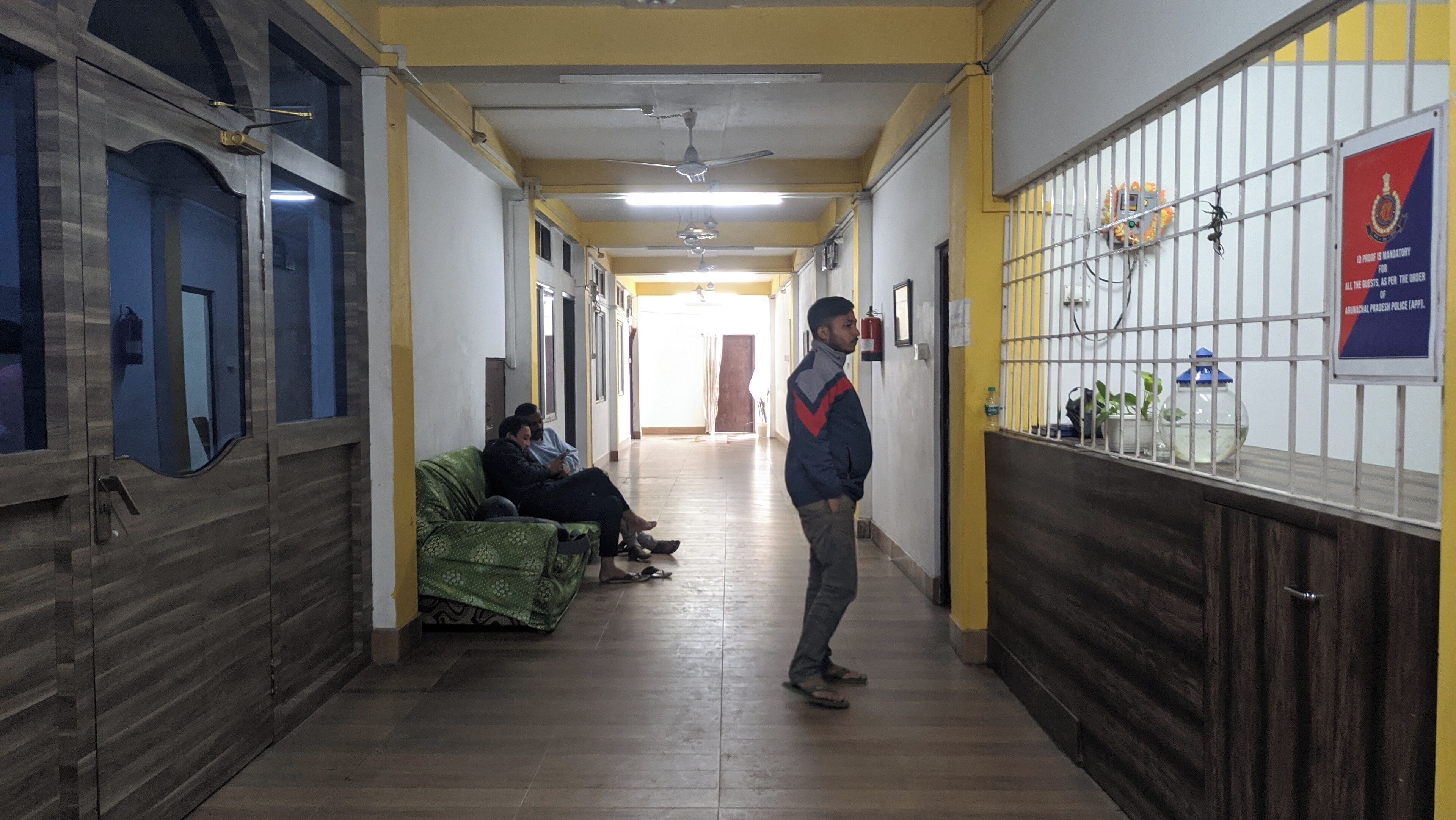 A hallway with a person standing, a bench with two people sitting, and a wall with a sign.