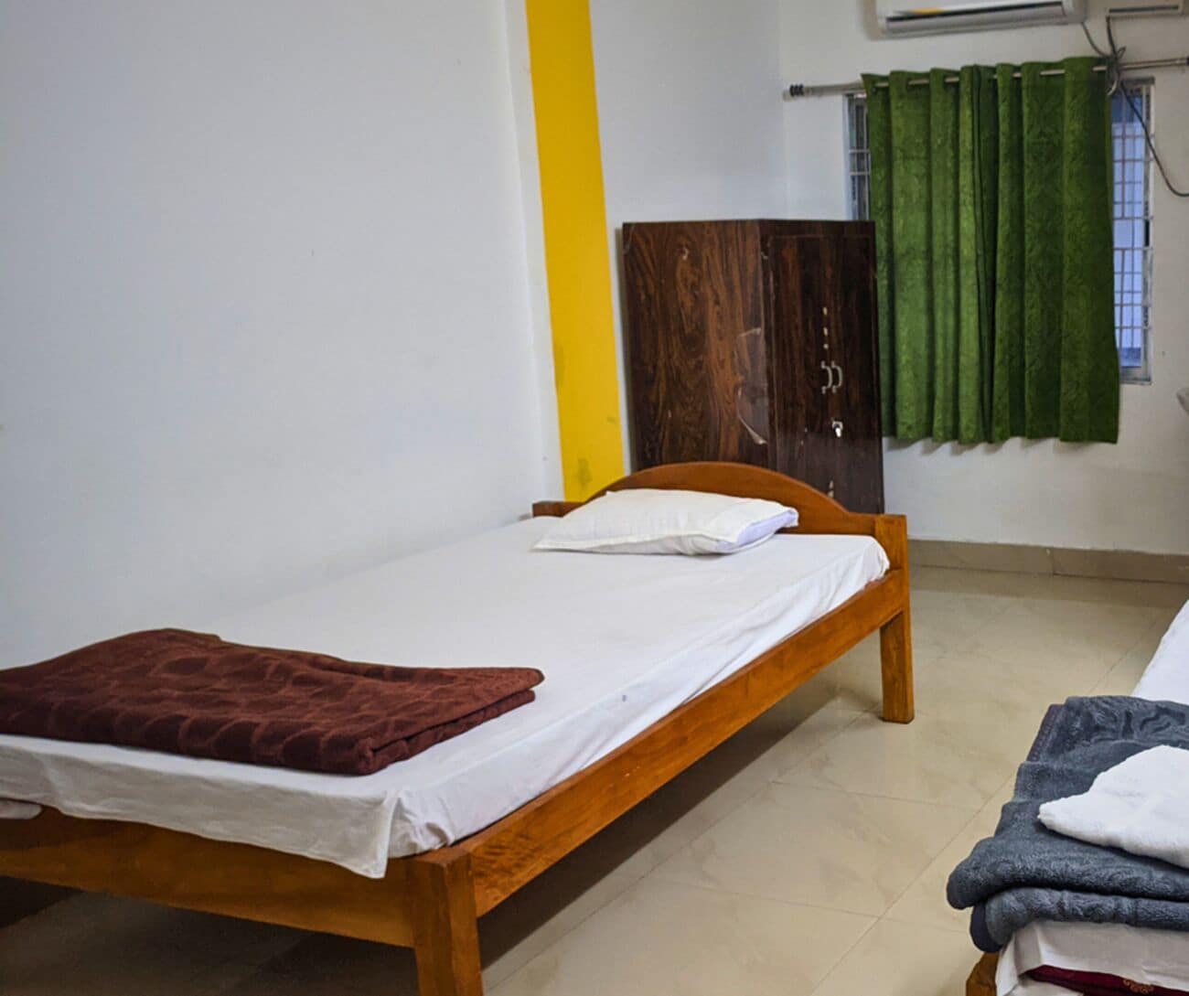 A single bed with a wooden frame, a white mattress, and a brown blanket.