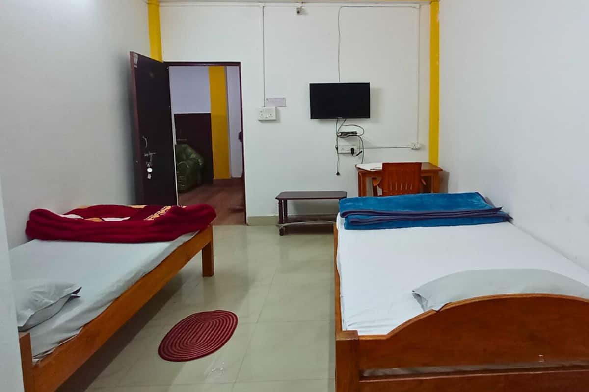 A room with two wooden beds, a television, a small table, and a bench.
