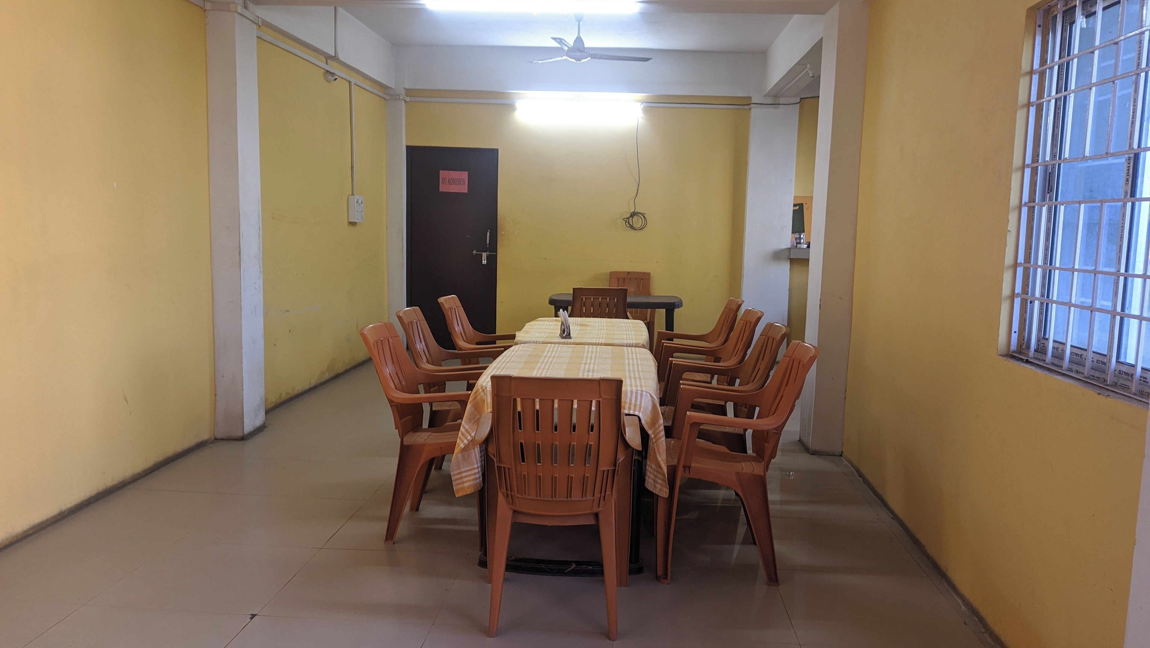 A dining area with a table set for four, surrounded by six chairs, in a room with yellow walls and a ceiling fan.