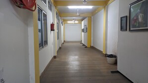 Ein langer, schmaler Korridor mit Holzboden, gelben Wänden und weißen Decken. Auf der linken Seite befinden sich Fenster, ein an der Wand befestigter Feuerlöscher und ein Mülleimer am Ende des Ganges.