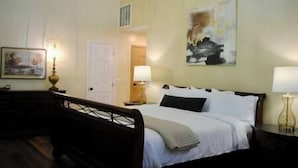 A hotel room with a bed, bedside lamps, a door, and a painting on the wall. - Magistrate Rm, The Lodge at Old City Hall (Jefferson City)