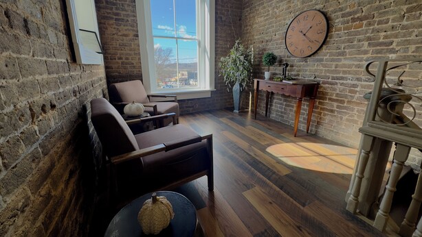 A cozy room with a brick wall, a large window, a clock, and a wooden floor. - Magistrate Rm, The Lodge at Old City Hall (Jefferson City)