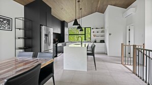 A modern kitchen with a central island, black chairs, and a dining table. - Eastman - Spa - Zénitude (Eastman)