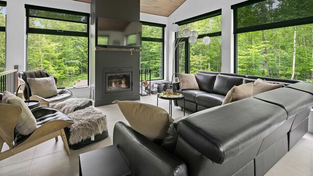 A modern living room with a fireplace, leather sofas, and large windows offering a forest view. - Eastman - Spa - Zénitude (Eastman)