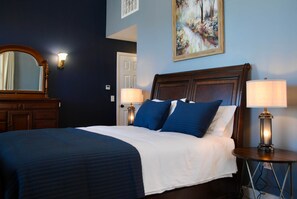 A hotel room with a large bed, two bedside lamps, a dresser, a mirror, and a painting on the wall. - Kinder Rm, The Lodge at  Old City Hall (Jefferson City)