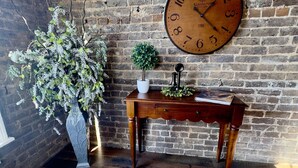 A brick wall, a wooden bench, a potted plant, and a large wall clock. - Kinder Rm, The Lodge at  Old City Hall (Jefferson City)