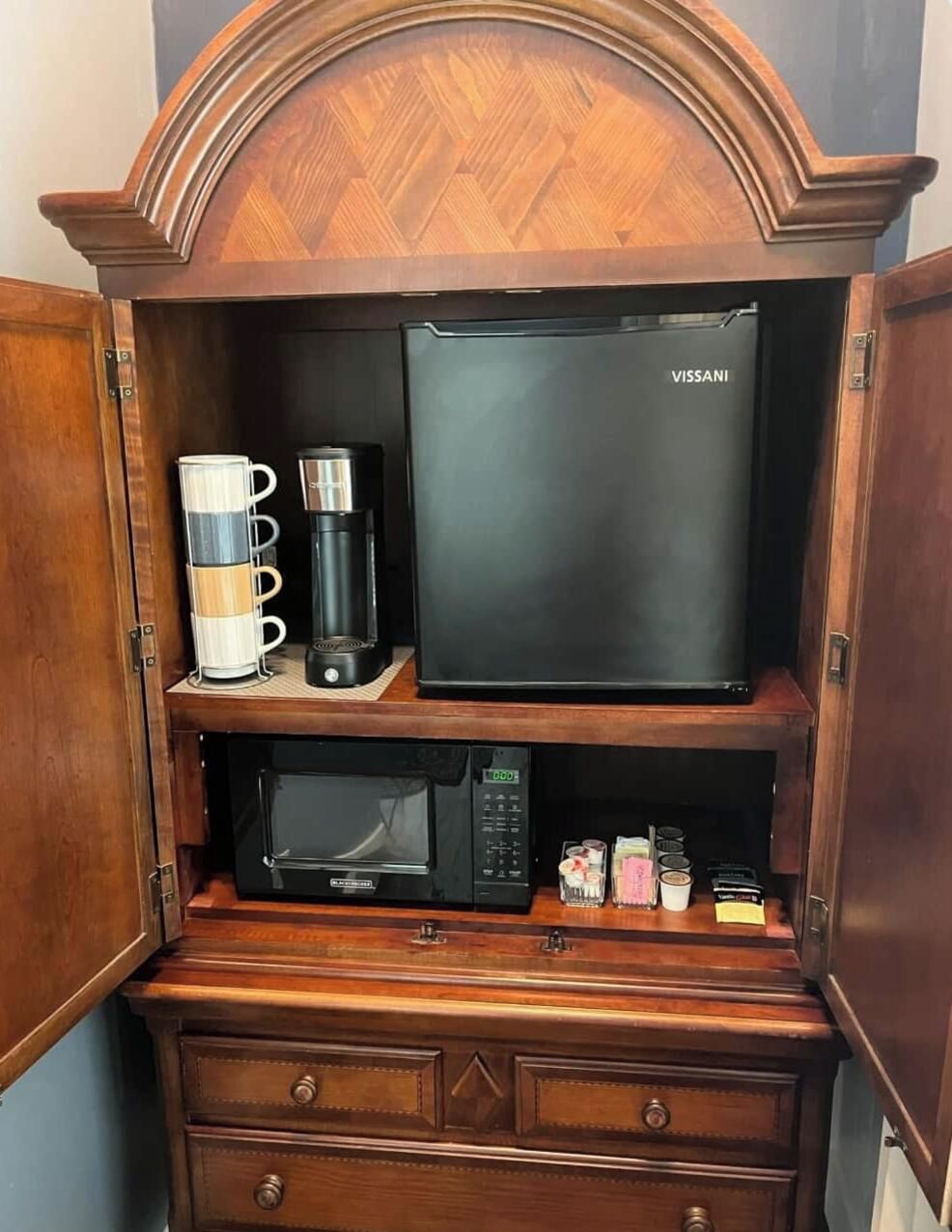 Eine kleine Küchenzeile mit einer VISSANI-Kaffeemaschine, einer Mikrowelle und einem kleinen Kühlschrank.