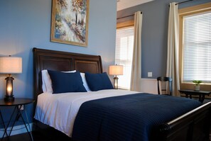 A hotel room with a bed, two bedside lamps, a painting on the wall, and a window with curtains. - Kinder Rm, The Lodge at  Old City Hall (Jefferson City)