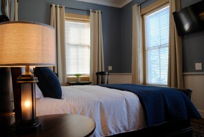 A hotel room with a bed, a bedside table, a lamp, a chair, and a TV.