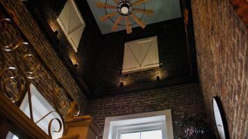 Une pièce avec un mur en briques, un ventilateur de plafond en bois et une fenêtre avec des volets blancs.