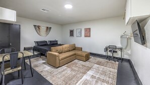 Une pièce moderne et bien éclairée, avec un canapé d’angle, une petite table à manger et un espace de travail compact.