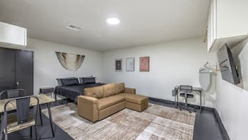 A modern, well-lit room with a sectional sofa, a small dining table, and a compact workspace.
