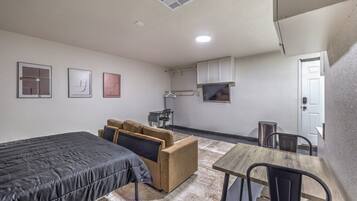 A compact room with a bed, a sofa, a small table, and a kitchenette.