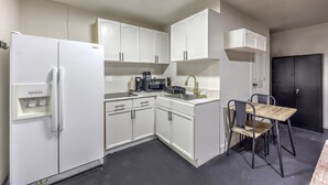 Une cuisine compacte avec des meubles blancs, un réfrigérateur noir, une machine à café et une petite table à manger avec des chaises.