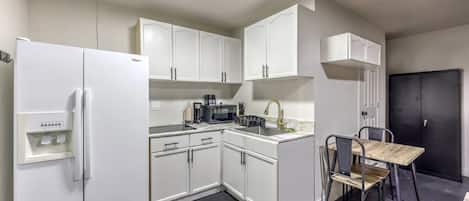 Una cocina compacta con armarios blancos, un refrigerador negro, una cafetera y un pequeño comedor con sillas.