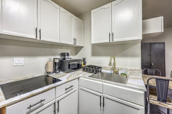 A compact kitchen with white cabinets, a stainless steel sink, a coffee maker, and a microwave.