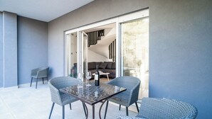 Un patio exterior moderno con puerta de vidrio que da a un espacio interior, con una mesa y sillas de comedor, una botella de vino y un sofá.