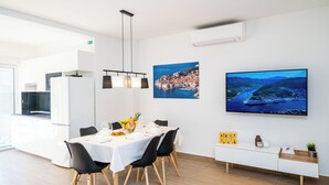 Un comedor moderno con una mesa blanca, sillas negras y un mueble blanco con televisor de pantalla plana.