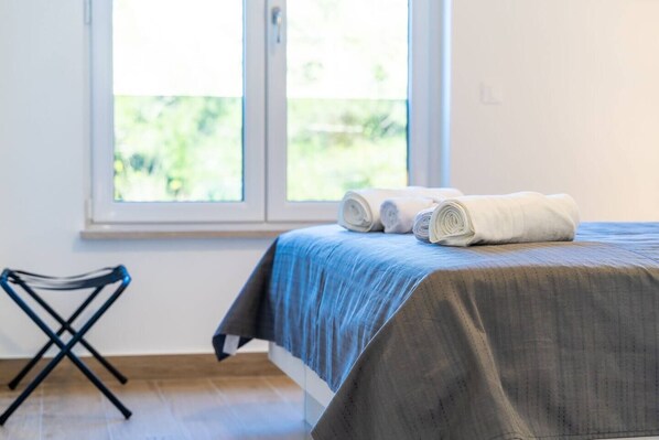 Una cama bien hecha con una colcha azul y toallas blancas enrolladas al lado.