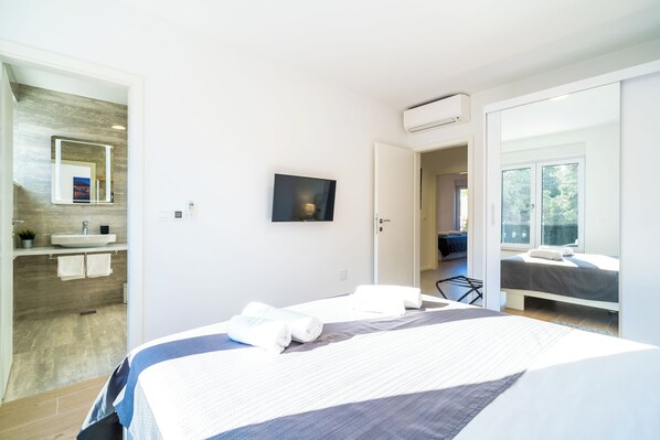 A modern hotel room with a large bed, a bathroom with a sink and mirror, and a view of the outdoors.