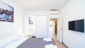 Habitación de hotel con una cama, un televisor de pantalla plana, un cuadro de una escena costera y una puerta que da al baño.
