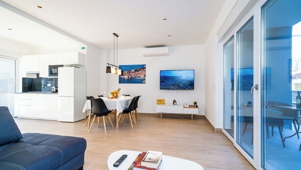 Una sala moderna con un sofá, un comedor con mesa y sillas, una cocina al fondo y un ventanal con vistas.